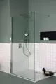 Duschbereich mit transparenter Glasscheibe, Regenbrause und Wandnischen, gestaltet in mattem Grün und weißen Fliesen. Ideal Standard-Produkte sind sichtbar.